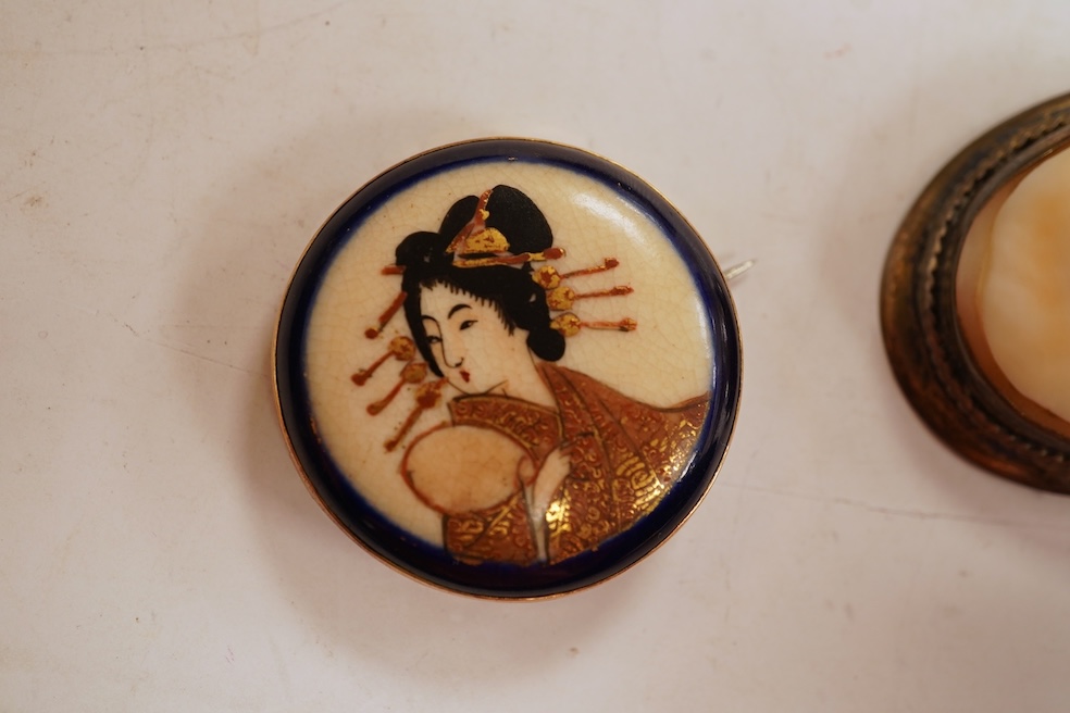 A Satsuma brooch, set with a circular Satsuma plaque depicting an oiran with gilded hair ornaments, mounted in 9ct gold, 3.3cm diameter, British hallmarks; together with an oval shell cameo brooch depicting a classical w